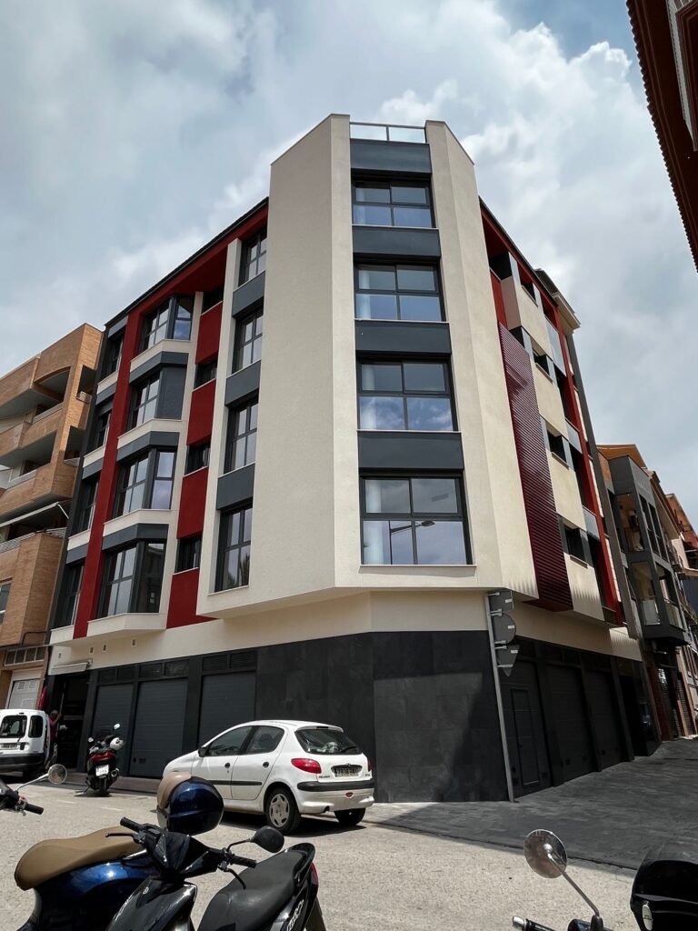 Edificio residencial moderno de varias plantas con balcones y fachada en rojo y blanco.