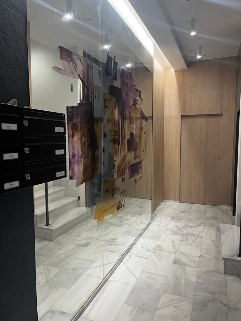 Portal de edificio con buzones, suelo de mármol y pared decorativa artística.